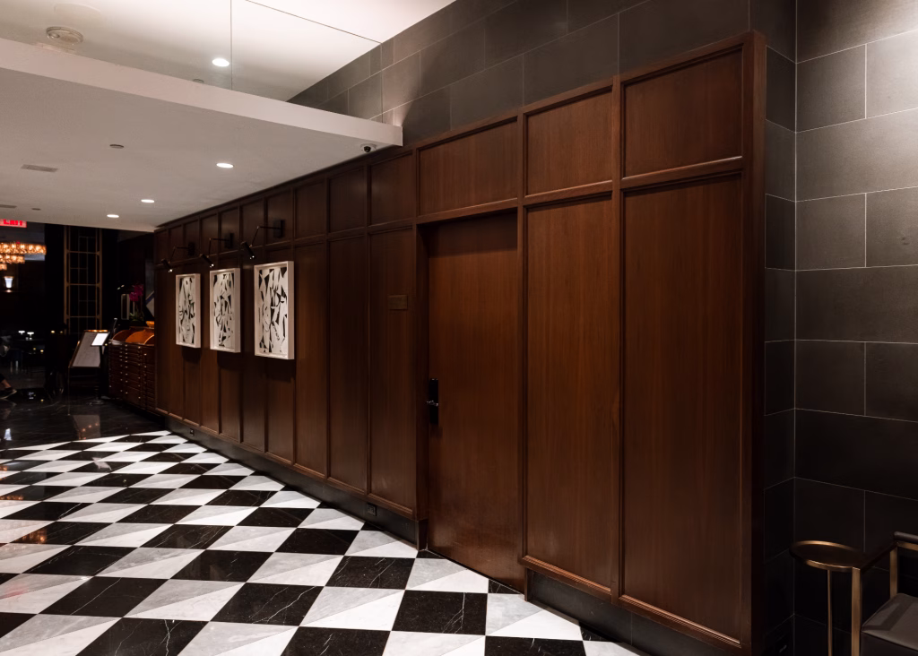 Custom wood wall paneling and architectural millwork at Hotel Belleclaire, featuring warm paneled details, framed artwork, and a black-and-white checkered floor.