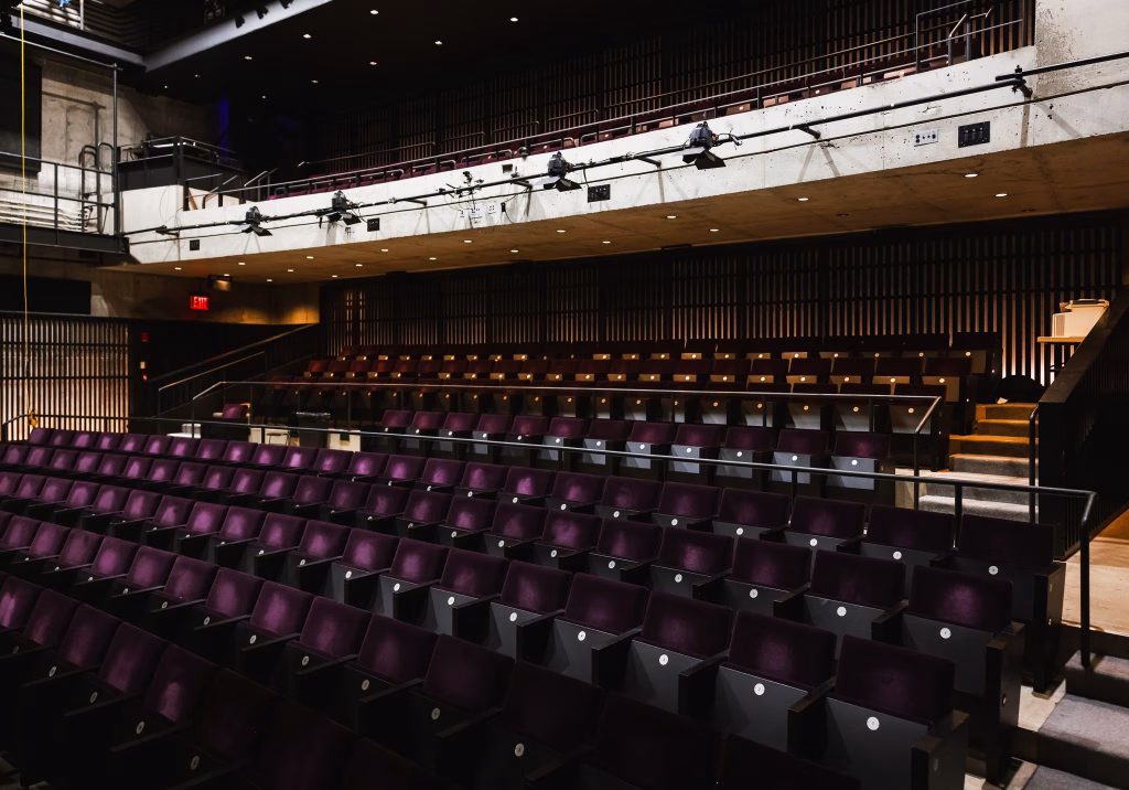 Interior of MCC Theater featuring rows of purple theater seating, custom acoustical wall panels, architectural millwork, and warm wood detailing in a modern performance space.
